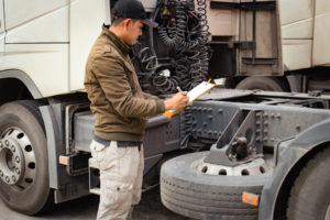 A man stands next to a truck with a clipboard, engaged in a commercial vehicle inspection process.