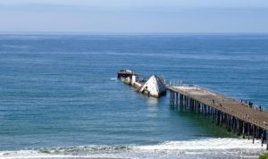 A scenic pier in Aptos, California, showcasing a boat moored on the ocean, with calm waves lapping at the structure.