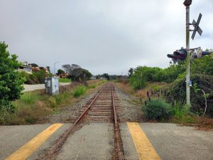 Railroad track in Aptos, California, featuring a crossing light and an approaching train in the background.