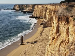 Cliffs rise majestically above a serene beach in Davenport, California, with a calm body of water reflecting the sky.