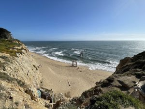 A breathtaking view of Davenport, California's beach from the top of a cliff, showcasing the ocean and sandy shoreline below.