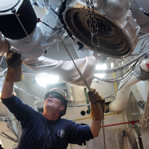 A technician is engaged in diesel engine maintenance on a large machine within a factory, highlighting industrial work practices.
