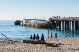 A group of individuals relaxes on the beach near a pier in Rio Del Mar, California, enjoying the sunny coastal scenery.