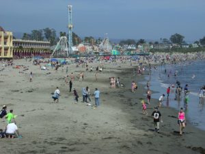 Crowds of beachgoers basking in the sun at Santa Cruz, California, with the ocean waves gently lapping at the shore.