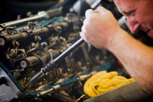 A man engaged in diesel truck repair, utilizing a wrench to fix the engine, demonstrating skill and concentration.