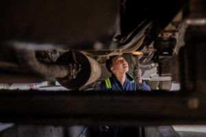 A man conducting a detailed inspection beneath a commercial vehicle to ensure compliance and safety standards.